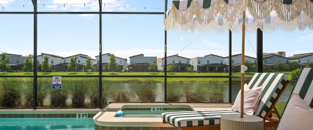 Aerial view of backyard with rectangular swimming pool, patio seating, lounge chairs, and manicured lawn bordered by hedges